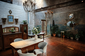Rustic dining room with vintage furniture, chandeliers, and potted plants. Wooden beams and exposed brick create a cozy ambiance perfect for gatherings and intimate dinners.