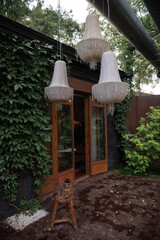 Elegant hanging lanterns adorn the entrance of a cozy garden, beautifully complementing the lush greenery. A rustic stool with a small decorative lantern adds charm.