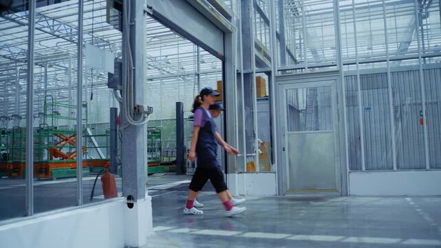 Two female agricultural technicians are exiting an industrial greenhouse