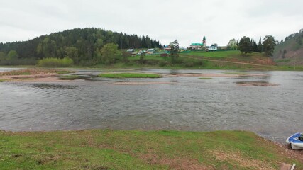 Imagine a tranquil riverside scene with kayaking gear, lush green grass, and dense forests, creating an ideal spot for outdoor enthusiasts to immerse themselves in natures beauty