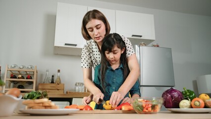 Smart caucasian mother and asian girl cooking together and chopping vegetable or preparing salad...