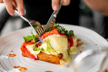 Close-up of a gourmet toast topped with melted cheese, roasted peppers, greens, and creamy sauce,...