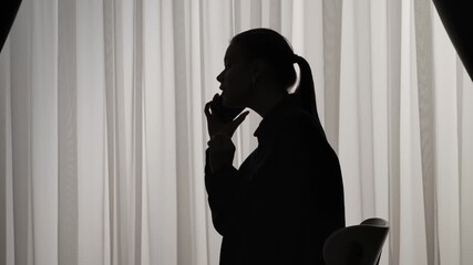 Silhouette of a Person Using Smartphone by Window Curtains