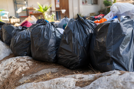 Black trash bags are stacked along a rocky area, ready for collection. Various discarded items can be seen, reflecting efforts to manage waste responsibly.