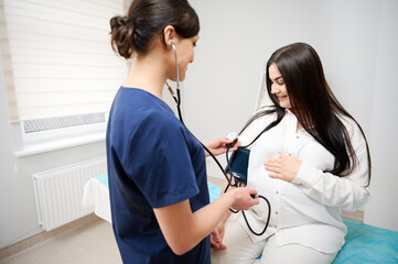Female doctor measuring blood pressure of pregnant woman in medical clinic. Obstetrician measuring...