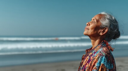 Elderly woman enjoying a peaceful moment on a sandy beach, standing with eyes closed and face lifted towards the sky, with gentle ocean waves in the background.