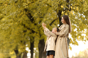 Family day. Happy smiling young mom soft hugs her adorable child daughter, looking up, having fun together outdoors at autumn park on fall holiday. Family look. Mother's day, children's day.