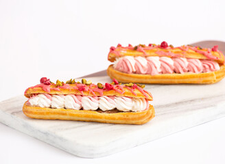Gourmet Pink Eclairs with Cream Filling, Pistachios and Dried Raspberries on marble board side view...