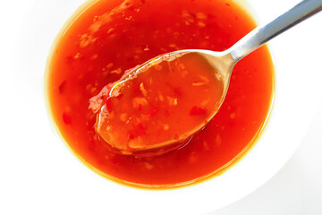 Sweet chilli sauce on spoon in a white bowl.