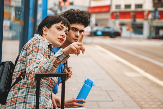Young adults waiting at a bus stop while engaged in conversation on a sunny day, showcasing city life and urban culture - Powered by Adobe