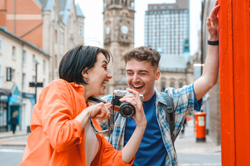 Young couple enjoying a sunny day in the city as one captures the moment using a camera while playfully posing in front of a red pillar