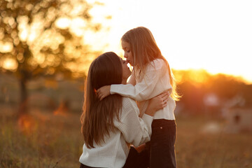 Family day, mother's day. Happy smiling young mom and adorable child daughter soft hugging, kissing and spending time together at autumn on sunset. Idyllic family having fun outdoors on fall holiday.