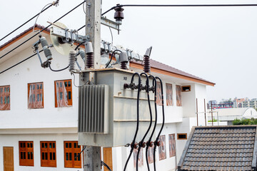 A distribution transformer mounted on a power line pole is located among residential buildings,...