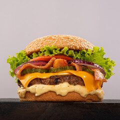 Juicy cheeseburger with melted cheddar cheese, crispy bacon, pickle slices, red onion, fresh tomato, and curly leaf lettuce, served on a sesame seed bun with a generous layer of mayonnaise.