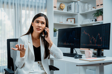Stressful young beautiful Asian businesswoman calling to broker on smartphone, analyze possible...