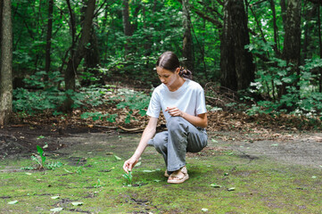 Teenage girl touches a sprout that has emerged from a path in a park