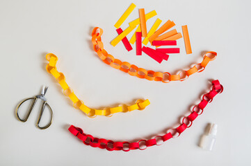 Multicolored handmade paper chains, scissors, glue and paper strips top view
