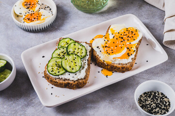 Cereal bread with cottage cheese, boiled egg and cucumber on a plate on the table