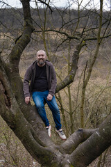 Man with beard seats on old big tree