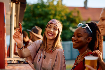Happy festival goer using payment card while buying drinks with her friends.