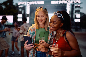 Happy women using app on smart phone while attending summer music festival.