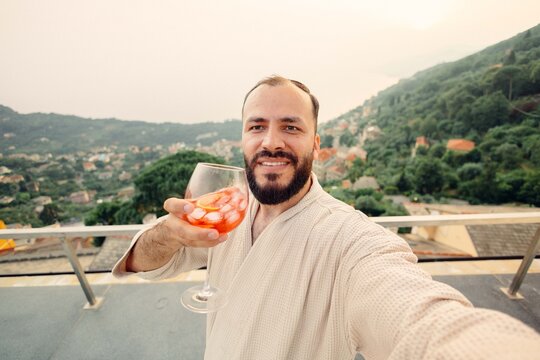 Tourist enjoying cocktail on balcony with scenic view of italian village