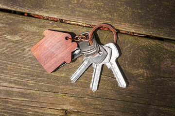 Apartment keys on table made of aged cracked wood. With wooden house shaped keychain 
