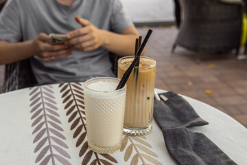 Two Iced coffee in glass cups. Man with smartphone on background. Cold drinks at the summer cafe