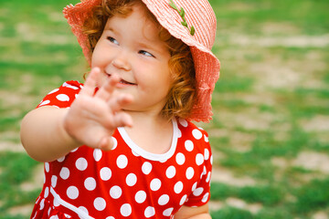 Smiling Child in Red Polka Dot Dress and Pink Hat Enjoys Sunny Day Outdoors in Green Park Setting