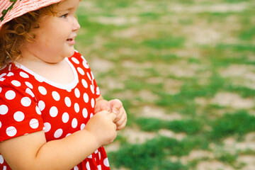 Smiling Child in Red Polka Dot Dress and Pink Hat Enjoys Sunny Day Outdoors in Green Park Setting