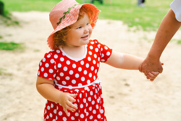 Little Girl in a Red Polka Dot Dress Enjoys a Sunny Day at the Park While Holding Hands With an Adult