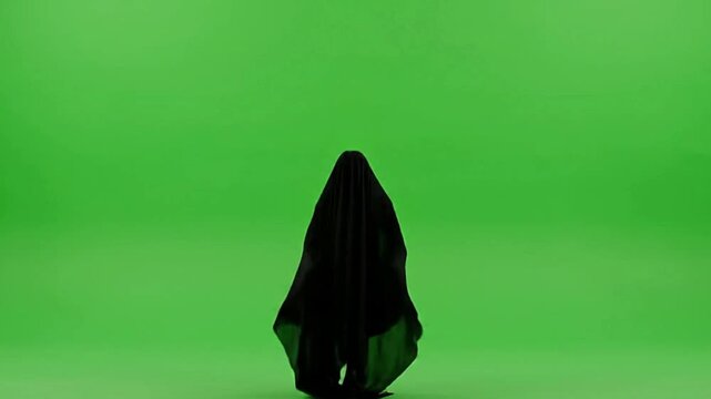 A black cloaked figure floats against a green screen backdrop