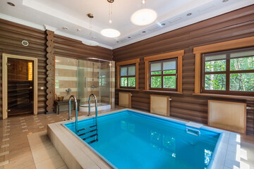 Relaxation space features a crystal-clear indoor pool surrounded by wooden walls and natural light....
