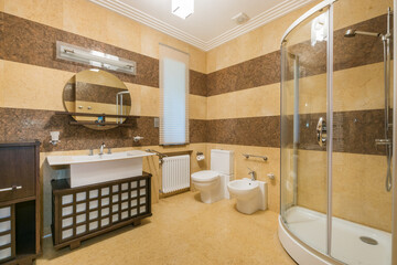 Stylish bathroom showcases a glass shower, contemporary vanity with a round mirror, and fitted fixtures against textured walls. Warm tones create a cozy atmosphere ideal for relaxation.