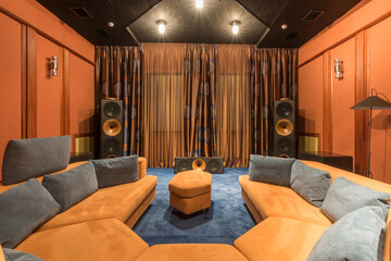 A stylish home theater features plush, colorful seating arranged around a central ottoman. Towering...