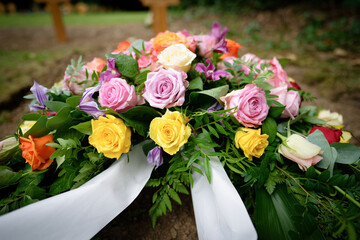 A small funeral wreath of pink, orange, yellow and white roses with wooden crosses in a blurred background on a modest urn grave in a cemetery