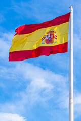 National flag of Spain flying in the wind; red and yellow national flag on blue sky background