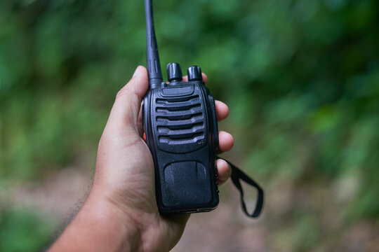 Hand holding a black two-way radio in a forest, focused shot of communication equipment on a soft, blurred green background, connectivity and security in remote or outdoor environments