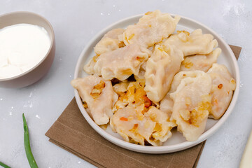 Homemade dumplings,vareniki,varenyky,pyrohy with stewed cabbage.Traditional ukrainian popular national dish,cuisine served with sour cream on gray background.