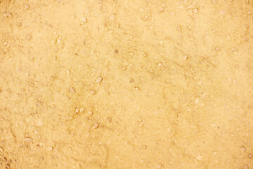 Dry ochre soil studded with weathered pebbles and fine sediment revealing intricate granular patterns under soft natural light