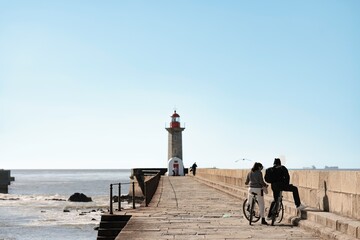 A couple stands with their bicycles on the pier leading to Farol de Felgueiras in Porto. Ocean...
