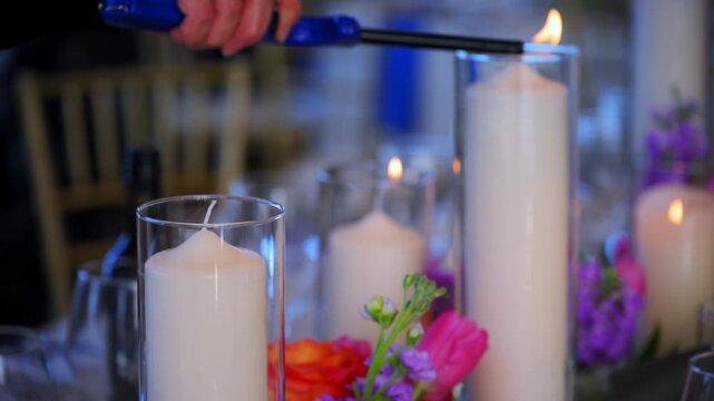 The close up scene of served table with glasses, plates, and candles at the celebration party. Female hand of wedding coordinator or party lighting candles on table
