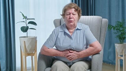 Fototapeta premium Senior woman holding her stomach, feeling unwell after eating. Allergy and gastric disease