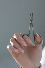 Manicure master's scissors in hand, showcasing perfect beige manicure in salon close-up