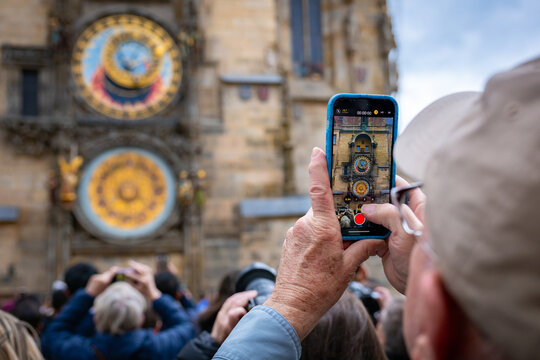 Elderly male tourist taking picture of the famous Prague astronomical clock on the Old Town Square in Czech Republic.