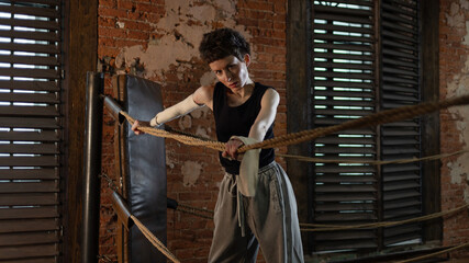 A woman in a boxing gym, portrait by the ropes, cinematic style, dark tones. Training and overcoming oneself, motivation