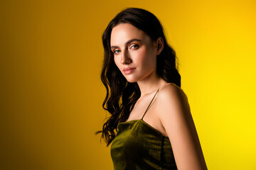 Chic young woman modeling elegant eveningwear on yellow backdrop with confident expression