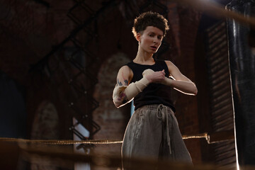 A woman in a boxing ring, wrapping an elastic bandage around her arms, preparing for boxing training. The photo is in a cinematic style, the light gives the mood to a sports motivational story about