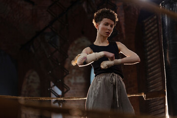 A woman in a boxing ring, wrapping an elastic bandage around her arms, preparing for boxing . The photo is in a cinematic style, the light gives the mood to a sports motivational story about self