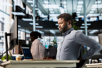 Black man CEO suffers from muscle cramps due to incorrect posture at the desk, dealing with neck...